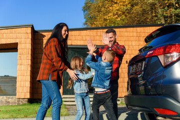 A happy family stands together near car and their house before going on a family vacation. © gorynvd