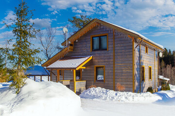 Two-storey private house in winter. Cottage on a Sunny winter day. Cottage on the background of the sky with clouds. Sunny winter day in the countryside.