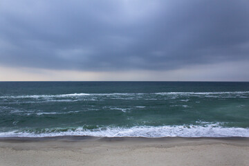 Dark grey stormy sky black sea horizon view with green water and sand 