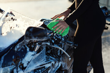 Obraz na płótnie Canvas close up of seductive young woman's hand washing stylish sport motorcycle and wipes it from pink foam at sunrise.