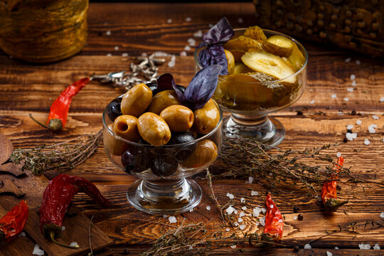 olives in glassware on wooden background with pickled cucumbers
