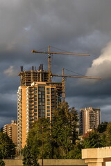 Construction of new high-rise buildings in Coquitlam City, industrial construction site, construction equipment, two construction cranes on the background of stormy cloudy sky