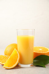 Tasty orange juice, fresh fruits and green leaves on light table