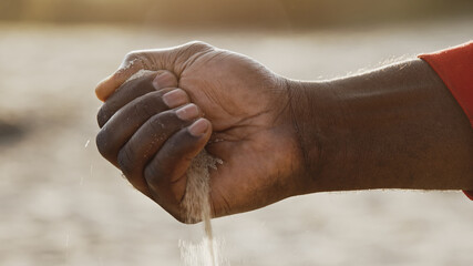Close up, black man hand pouring sand. Low angle shot. High quality photo