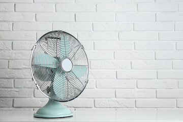 Electric fan on table near white brick wall, space for text. Summer heat