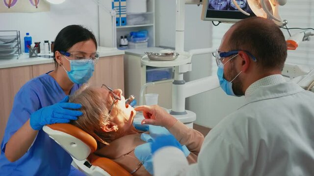 Dentistry doctor and nurse preparing patient for removing crowns. Orthodontist technician wearing protection mask treating teeth of senior woman in stomatological office lying on chair with open mouth