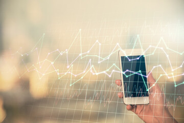Double exposure of forex chart sketch hologram and woman holding and using a mobile device. Stock market concept.