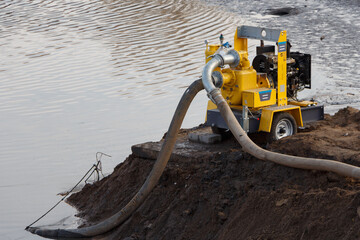 Professional electric pump stands by the water with submerged hoses.