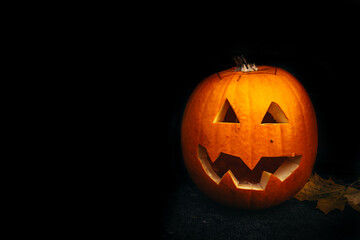 Funny halloween carved pumpkin into face expression, black background with copy space, creative squash carving for ghost night and trick or treat hunt, pumpkin surrounded by yellow autumn leafes