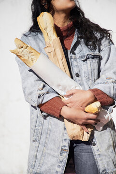 mujer morocha sosteniendo par de baguettes para llevar en campera de denim y bufanda sobre fondo blanco plano americano
