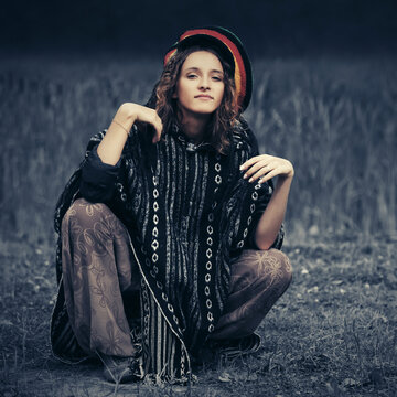 Young fashion hipster woman in rasta poncho sitting on the ground outdoor