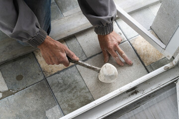 Close up on hands of unknown senior man craftsman using hammer to adjust and lay ceramic tiles on...