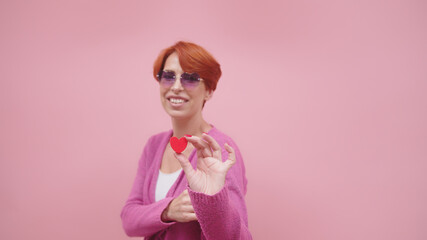 Middle aged redhead woman holding heart shape. Isolated on purple background. High quality photo