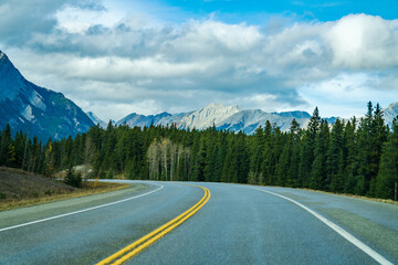 Rural road in the forest with mountains in the background. Alberta Highway 11 (David Thompson Hwy), Jasper National Park, Canada.