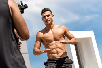 Handsome muscular man fitness influencer recording exercise video clip ourdoors on rooftop, home...