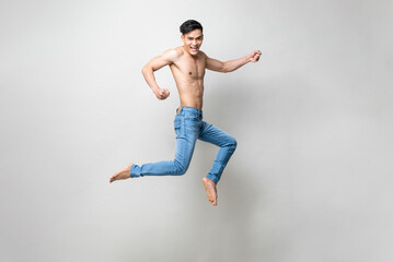 Energetic attractive shirtless Asian man smiling and jumping in light gray studio isolated background