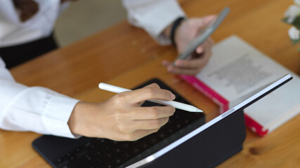 Female hand working with digital tablet and smartphone on wooden table