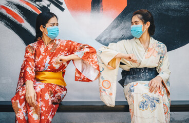 Two Asian woman in Kimono dress bump elbows for greeting during coronavirus pandemic.