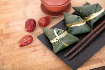 A plate of zongzi and red dates for the Dragon Boat Festival on a cutting board, chopsticks and a bowl of tea