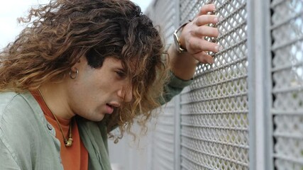 young desperate man just out of a bad situation leaning against a grate