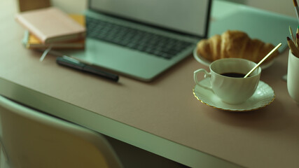 Breakfast meal with coffee cup and croissant on workspace with laptop and stationery
