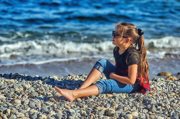 Portrait of a little girl in jeans and t-shirt resting on the seashore .