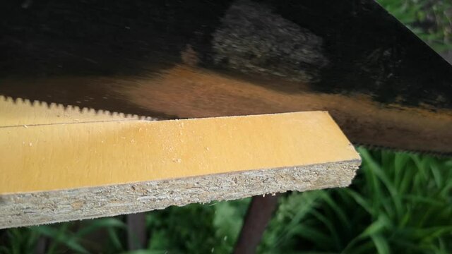Man saws a wooden board with a hand saw