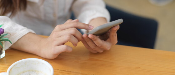 Female hands using smartphone on wooden table in coffee shop