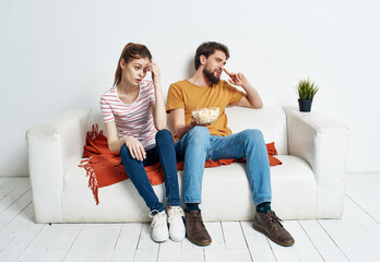 cheerful man and woman on the couch with popcorn and red plaid flower in a pot emotions