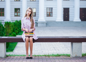 Young beautiful blonde sitting on a bench with books