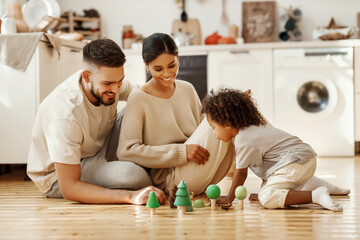 Diverse parents playing with son in kitchen.