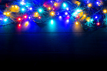Christmas lights background with free text space. Glowing colorful Christmas lights on wooden background. New Year. Multi color lights for decorate event.