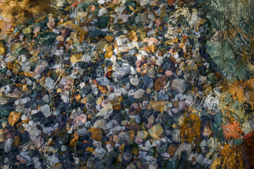 Rocky bottom of mountain stream, close-up. Colorful stones under clear water. Beautiful distortion background. Natural mosaic of small stones. Image for ceramic tile design, bathrooms.