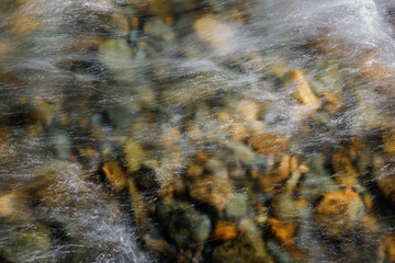 Rocky bottom of mountain river through the clear water, selective focus, blurring the image. Cristal water in the stream shimmers in sunlight. Stone background.