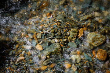 Rocky bottom of mountain river through the clear water, selective focus, blurring the image. Cristal water in the stream shimmers in sunlight. Stone background.