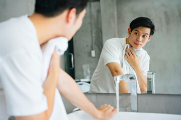 Obraz premium Young man washing and cleaning face with towel in bathroom.