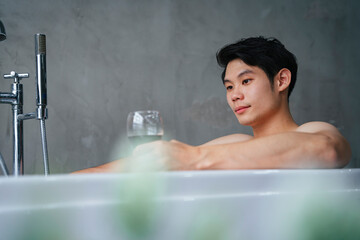 Asian man enjoy taking bath in a tub with red wine.
