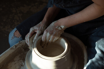 Hands of woman working with pottery wheel and making ceramic chamotte vase on it. dark and light