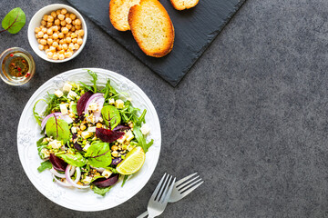 Fresh vegetable salad with beets, arugula, red onions, sorrel, chickpeas, cheese in a white plate on a black background. Top view