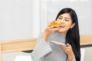 Beautiful woman eating delicious pizza on bed.