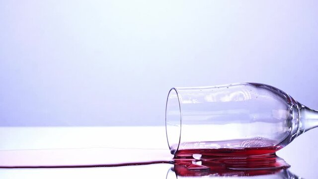 Wineglass tilted down, red wine spilled on the table, white background