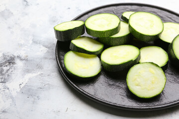 Plate with fresh zucchini squashes on light background