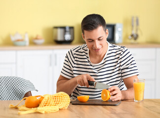 Fototapeta na wymiar Handsome man cutting ripe oranges in kitchen