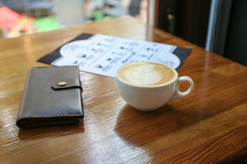 Cup of hot coffee, wallet and menu on table in cafe