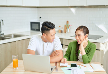 Obraz premium Photo of cheerful loving young couple using laptop and analyzing their finances with documents. Look at papers.