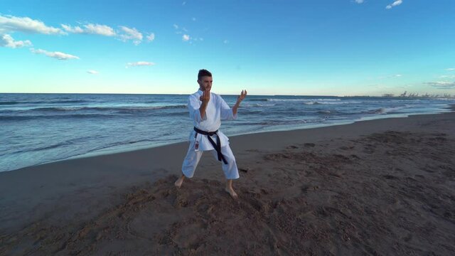 Karate fighter practicing a kata on the beach at sunset. Karate fighter practicing technique kicking and punching hard and fast. Traditional karate Wado Ryu. 4K video