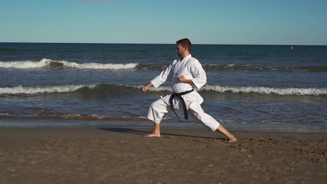 Karate fighter practicing katas on the beach at sunset. Karate fighter practicing technique outdoors. Wado ryu style. Truck left camera movement recorded in slow motion. Chinto