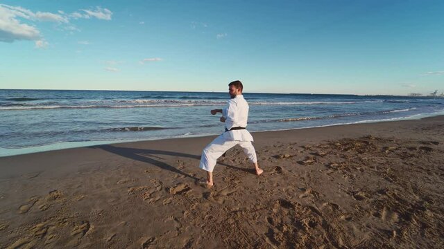 Karate fighter practicing katas on the seashore at sunset. Karate fighter practicing technique with blows, defenses and kicks. Karate Shitu Ryu. 4K video