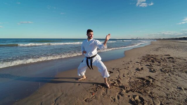 Karate fighter doing fast and powerful movements on the seashore at sunset on the beach. Karate fighter doing katas on the beach