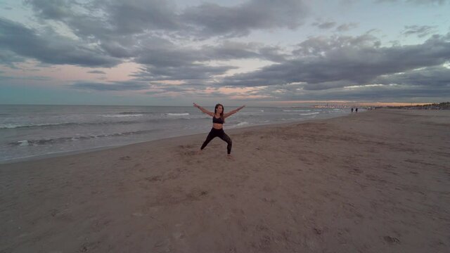 Woman practice yoga at beach with a beautiful sunset and clouds. Bird of paradise. Extended angle, Warrior poses, Mountain pose. utthita parsva konasana, tadasana, virabhadrasana, eka pada utkatasana